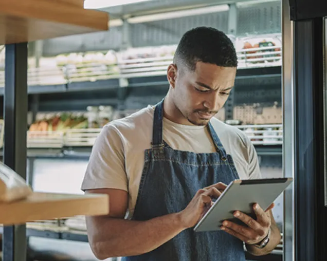 Grocery store employee using a tablet in front of a refrigerated produce section in a grocery store